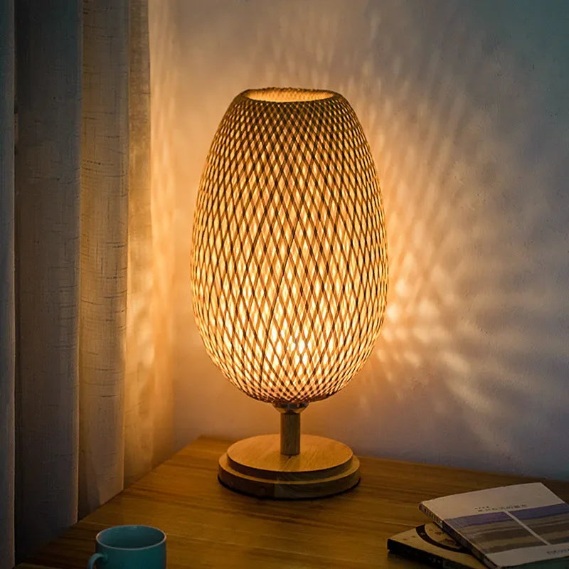 Woven table lamp casting a warm glow on a wooden surface with a book and mug.